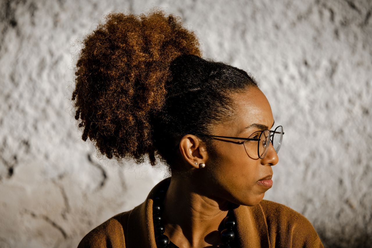 footer-01 Portrait of a fashionable woman with a curly hairstyle, wearing glasses and a necklace.