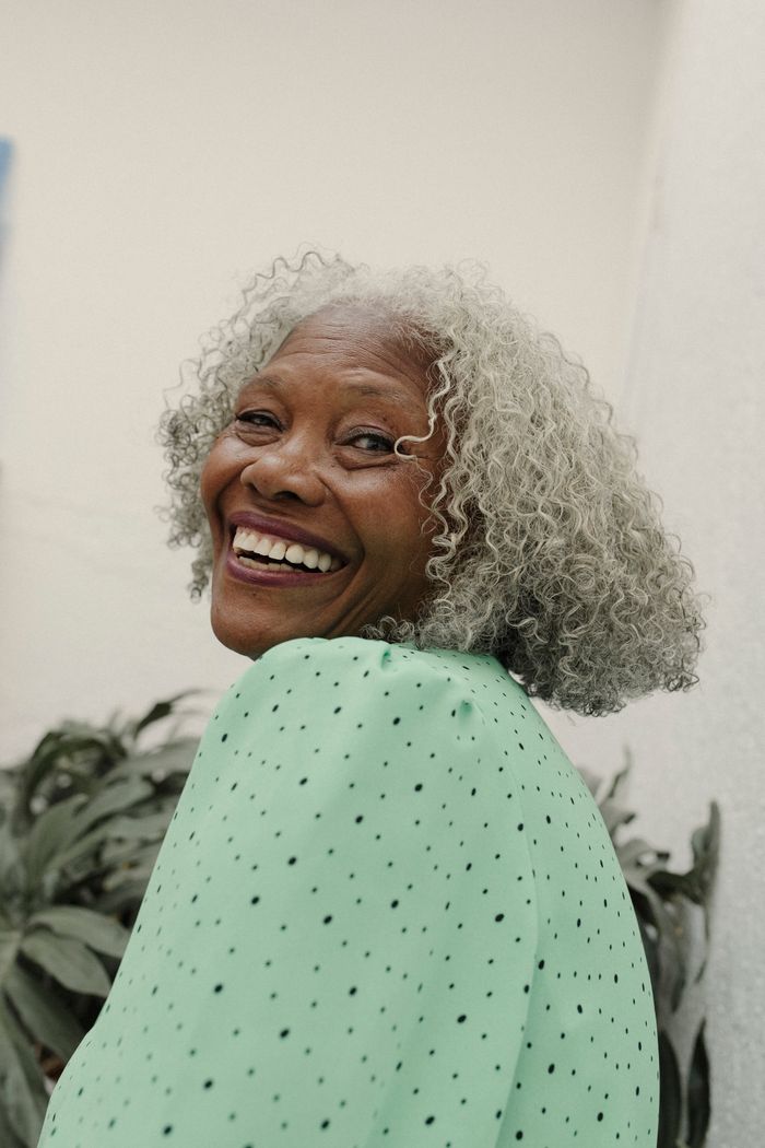 about-hero-03 Radiant senior woman smiling outdoors in a vibrant green outfit.