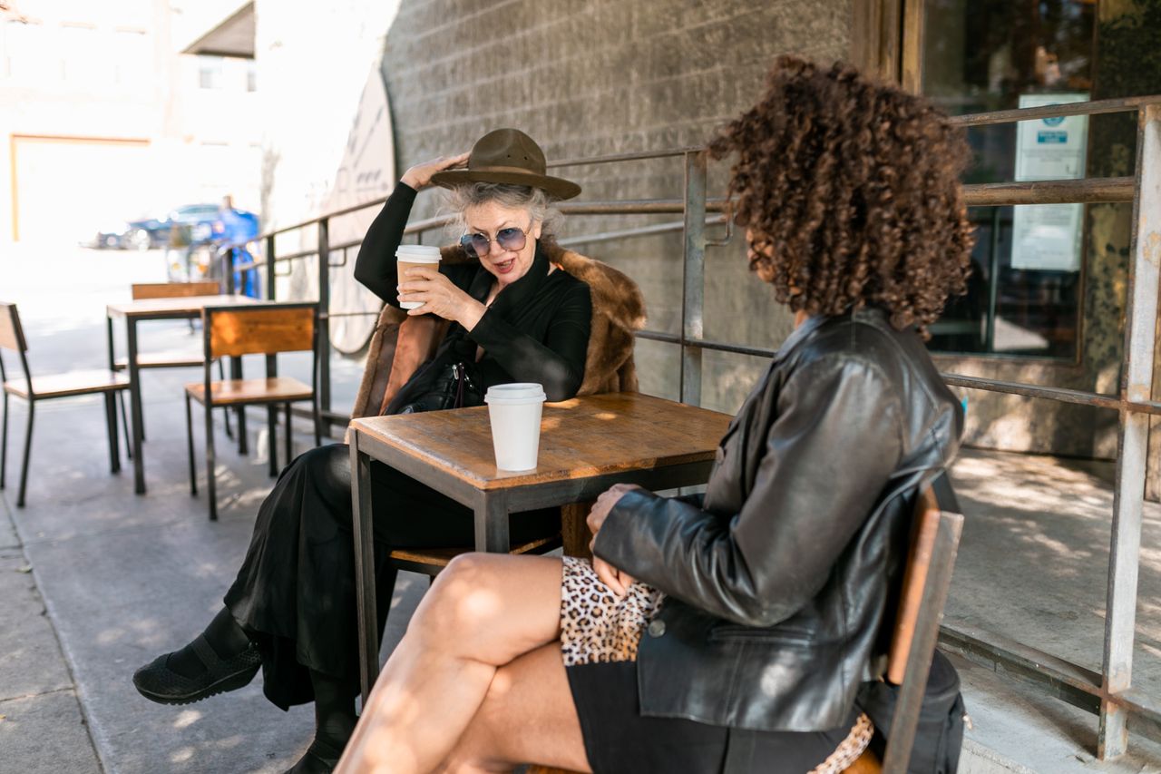home-hero-01 Two stylish women enjoying coffee outdoors, capturing a moment of leisure and friendship.