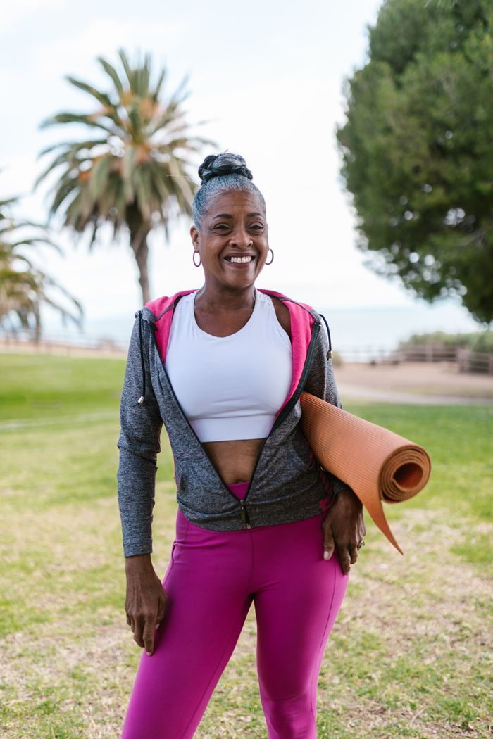 work-02 Happy senior woman holding a yoga mat, enjoying an outdoor workout session on a sunny day in the park.