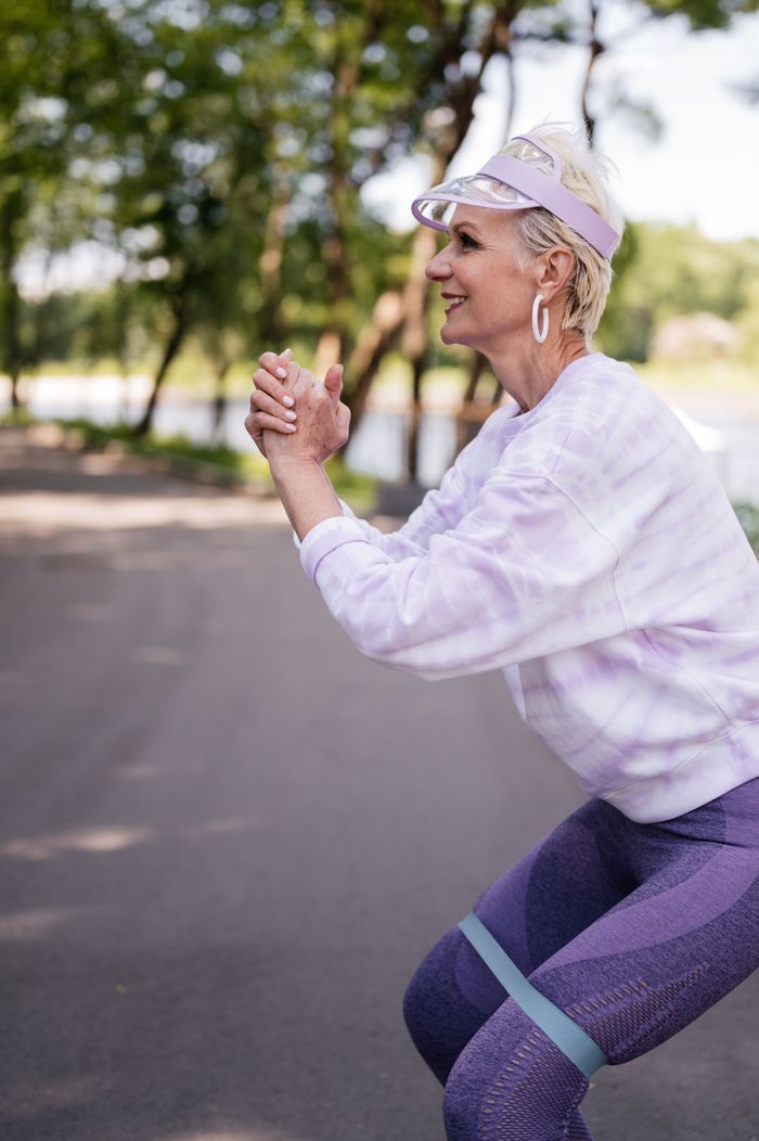 work-01 A senior woman performing exercises with a resistance band in a park, promoting a healthy lifestyle.